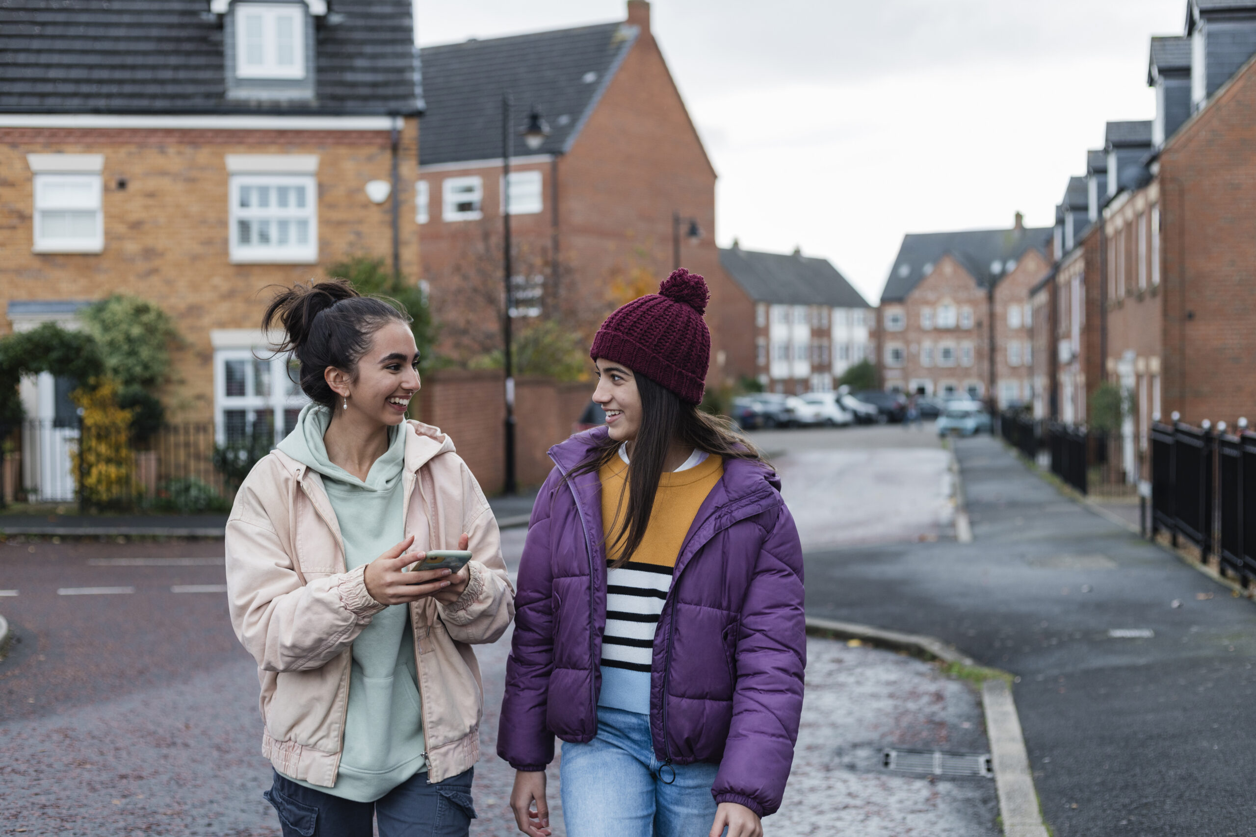 Two foster sisters spending time together outdoors, laughing and talking on a walk, using a mobile phone together. They are in the North East of England.