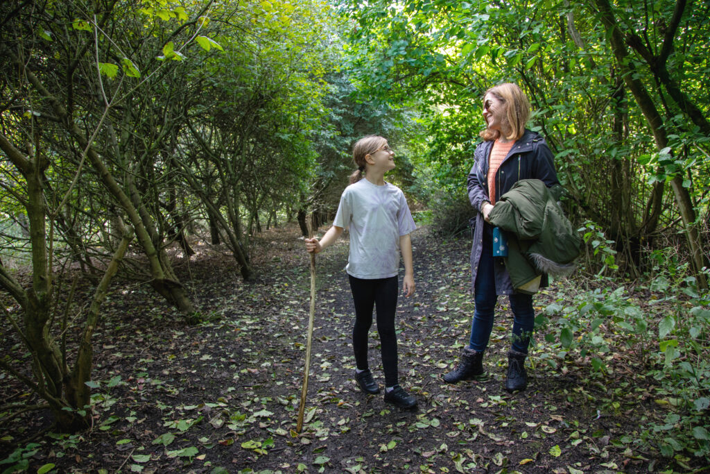A woman and a child with a walking stick on a woodland path